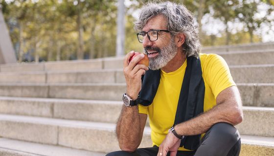 Entspannter älterer Mann beißt in einen Apfel.