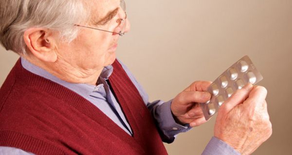Älterer Mann mit Blisterpackung schaut auf Blisterpackung mit Antibiotika in seinen Händen