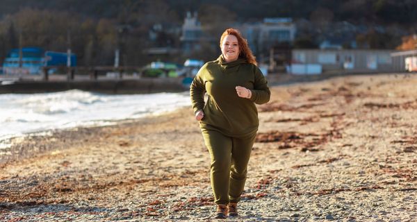 Übergewichtige Frau, joggt am Strand.
