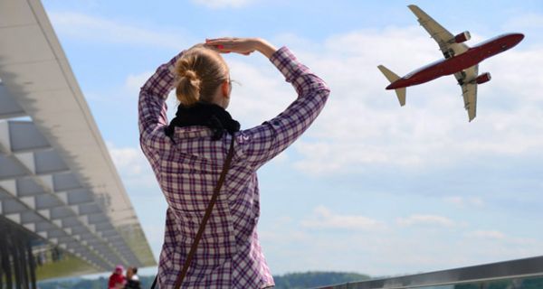 Szene vor Flughafen, Frau von hinten, Karohemd, Jeans, beobachtet Flugzeug beim Abflug