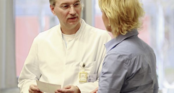 Arzt im Gespräch mit einer Patientin, in der Hand hält er ein Rezept