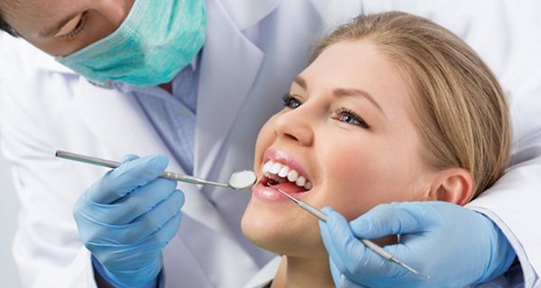 Nahaufnahme Gesicht: Junge Frau im Zahnarztstuhl, Zahnarzt schaut in ihren Mund mit Spiegel und Haken