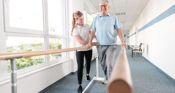 Physiotherapeutin hilft älterem Mann bei Übungen.