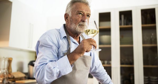 Älterer Mann steht in der Küche und trinkt Weißwein
