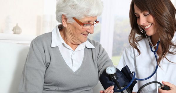 Seniorin bekommt von jüngerer Ärztin den Blutdruck gemessen
