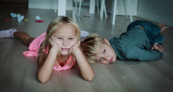 Zwei Kinder, liegen gelangweilt und deprimiert auf dem Boden.
