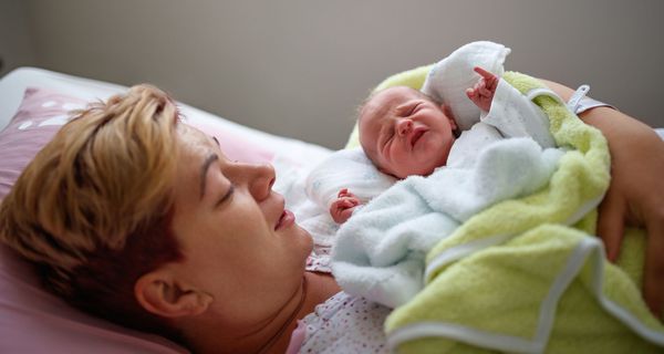 Junge Frau mit Neugeborenem im Arm.