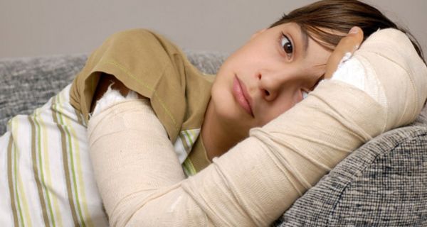 Nahaufnahme: dunkelhaariges Kind, ca. 12 Jahre, auf Couch liegend, traurig schauend, rechter Arm eingegipst