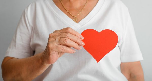 Ältere Frau, hält sich ein rotes Herz vor die Brust.