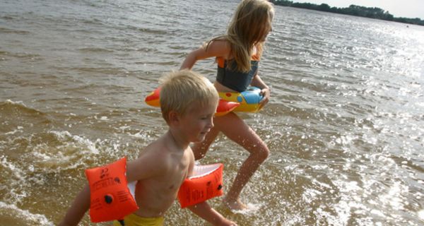 Zwei Kinder mit Schwimmflügeln laufen am Strand.