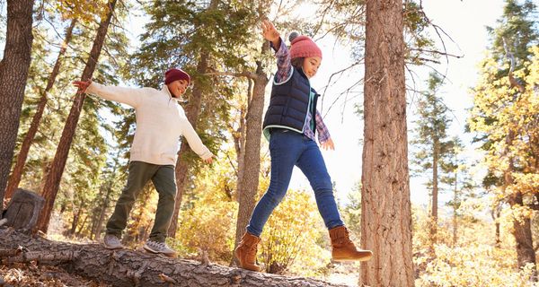Zwei Kinder, balancieren im Wald über einen Baumstamm.