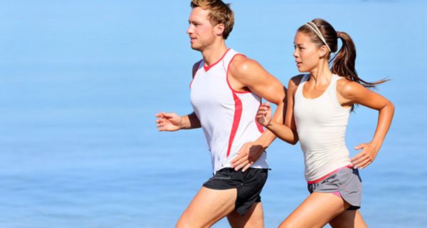 Frau und Mann um die 30, Profilbild, rechts, laufen in leichter Sportkleidung (Shorts, Sportshirts ohne Ärmel) schwitzend; Hintergrund Wasser