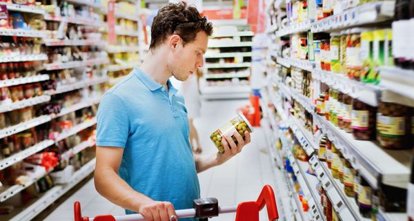 Junger Mann im Supermarkt, betrachtet das Etikett eines Lebensmittels.