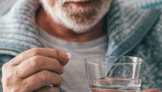 Älterer Mann, nimmt eine Tablette mit einem Glas Wasser.