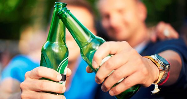 2 männliche Jugendliche, Hintergrund, unscharf, prosten sich zu: Vordergrund 2 Bierflaschen
