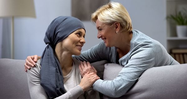 Krebspatientin, wird von hinten von einer älteren Frau umarmt, beide lächeln.