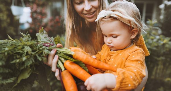 Junge Mutter mit kleinem Mädchen, das Karotten in der Hand hält.
