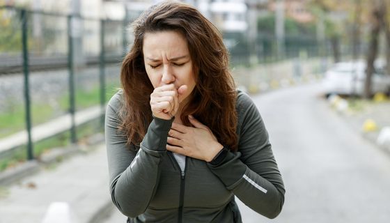 Frau auf der Straße hustet heftig.