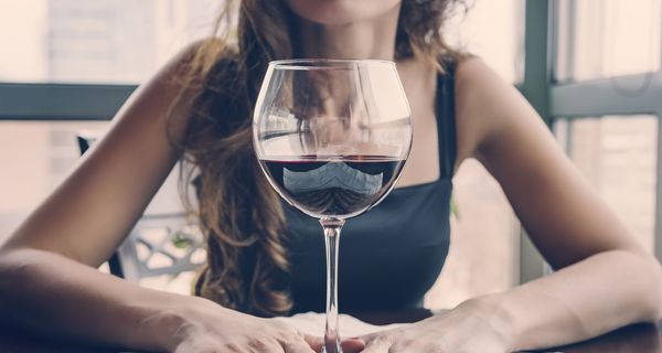Junge Frau, sitzt vor einem großen Glas Rotwein.
