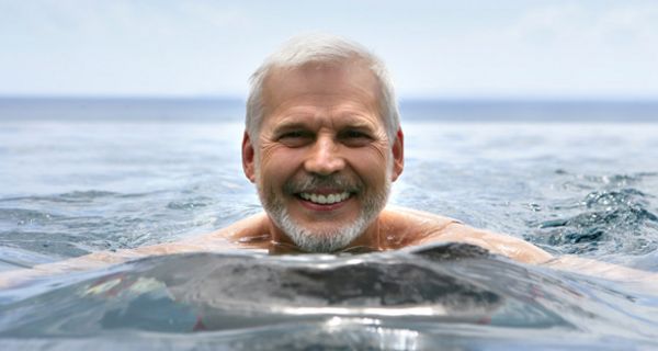 Portraitfoto, älterer Mann schwimmt lachend im Meer