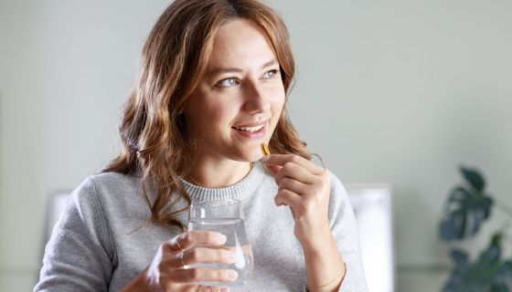 Junge Frau nimmt eine Kapsel, vermutlich Vitamin D, ein.