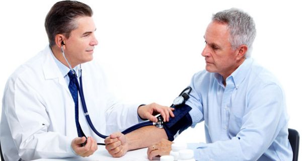 Ein Arzt sitzt einem älteren Patienten gegenüber und misst seinen Blutdruck.