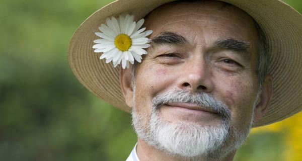 Lächelnder Mann mit Strohhut und Blume hinter dem Ohr.