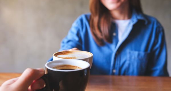 Mann und Frau, stoßen gemeinsam mit einer Tasse Kaffee an.
