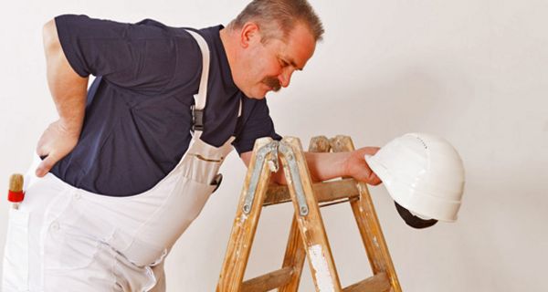 Bauarbeiter stützt sich an einer Leiter ab und hält sich den schmerzenden Rücken