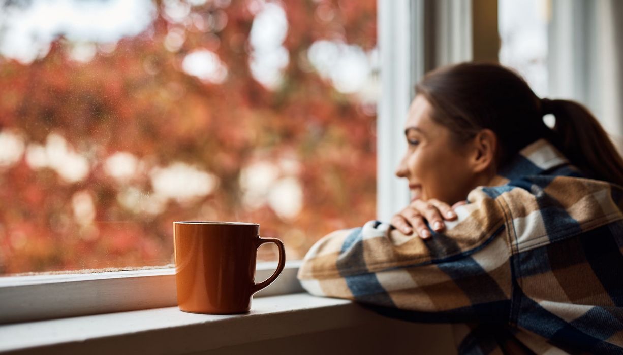 Junge Frau mit einer Tasse Kaffee, schaut aus dem Fenster.