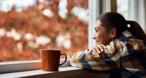 Junge Frau mit einer Tasse Kaffee, schaut aus dem Fenster.