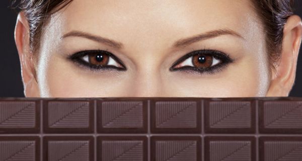 Eine junge Frau, deren Gesicht zur Hälfte von einer Tafel Schokolade verdeckt ist.