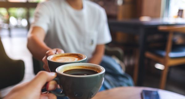 Zwei Männer, prosten sich mit einer Tasse Kaffee zu.