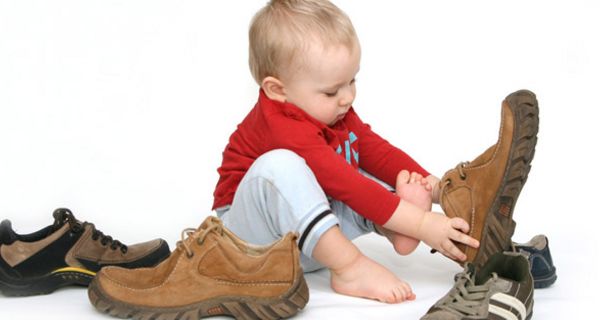 Kind spielt mit großen Schuhen.