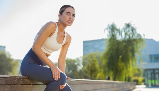 Junge Frau in Sportkleidung hält sich das Knie.