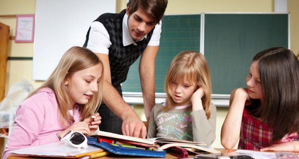 Älterer Schüler hilft drei Grundschülerinnen bei den Hausaufgaben.
