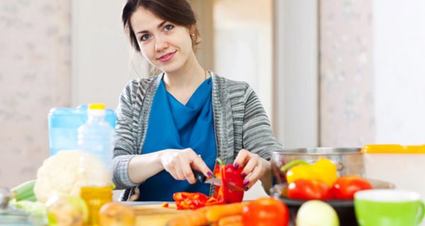 Junge Frau mit blauer Schürze beim Zubereiten veganer Mahlzeit in der Küche