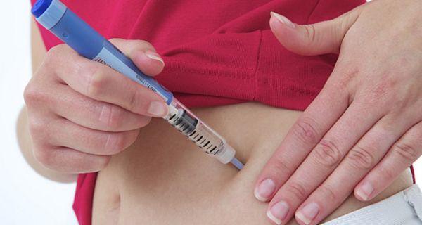 Fotoausschnitt Bauch, in den von einer Frauenhand Insulin gespritzt wird