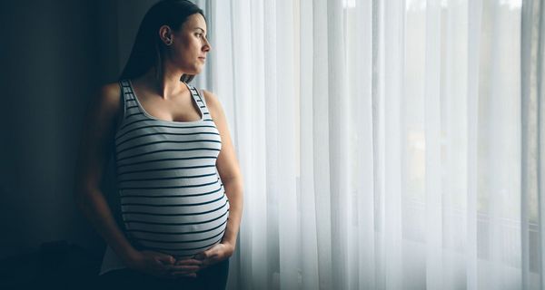 Schwangere Frau, schaut aus dem Fenster.