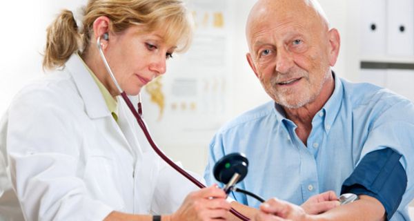 Älterem Mann wird von Ärztin der Blutdruck mit Oberarm-Manschette und Stethoskop gemessen