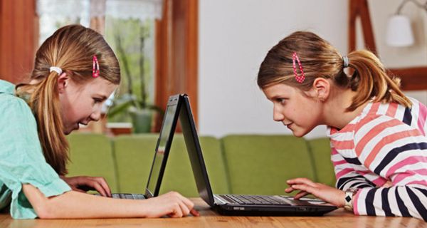 Zwei Mädchen sitzen sich mit Laptops gegenüber