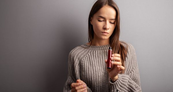 Junge Frau, hält eine E-Zigarette in der Hand und schaut diese fragend an.
