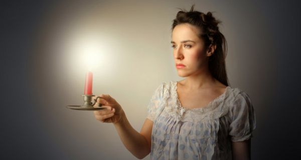 Junge Frau im Nachthemd trägt des Nachts eine Kerze vor sich her