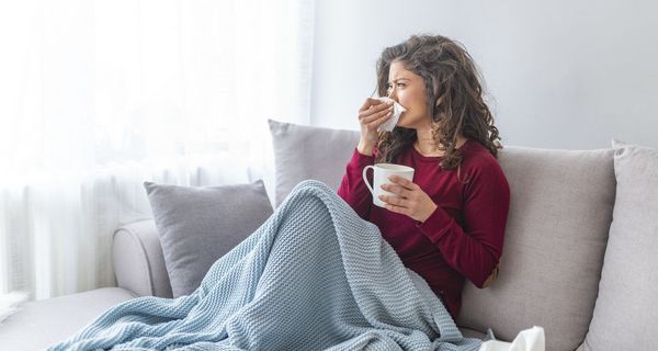 Frau mit Erkältung sitzt auf dem Sofa und putzt sich die Nase