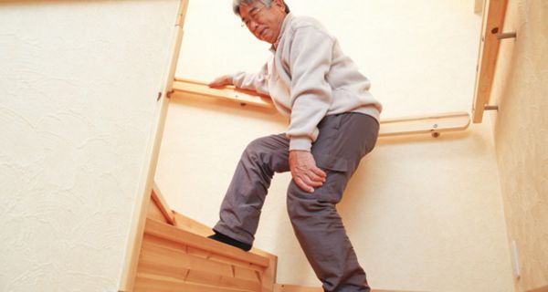 Asiatischer Senior steigt eine Treppe hinauf und hält sich die Hand ans schmerzende Knie