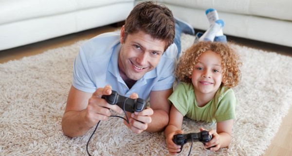 Junger Vater und kleiner Sohn liegen bäuchlings auf dem Teppich und spielen ein Videospiel