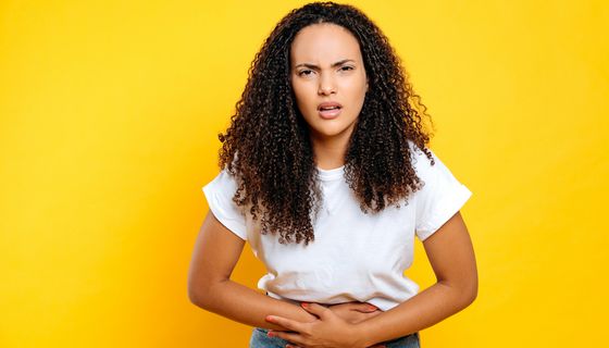 Junge Frau hält sich den Bauch und schaut genervt.