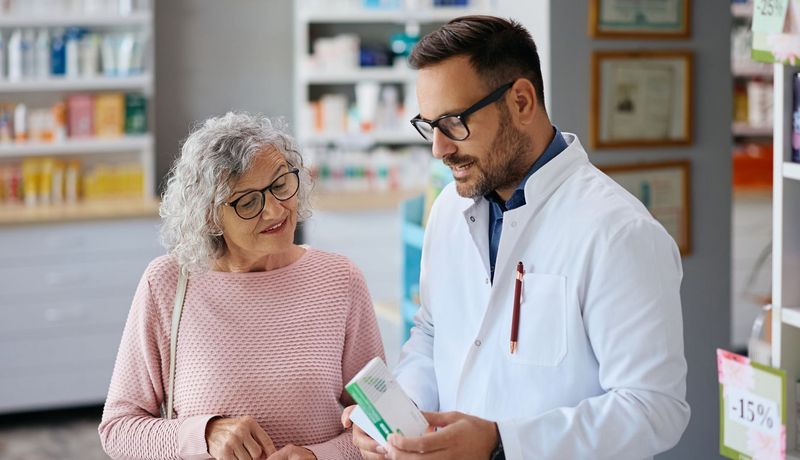 Ein Apotheker berät eine ältere Kundin zu einem Medikament.