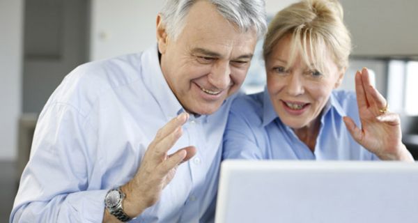Aufgeregt lachendes Paar in den 60ern schaut auf einen Laptop-Bildschirm