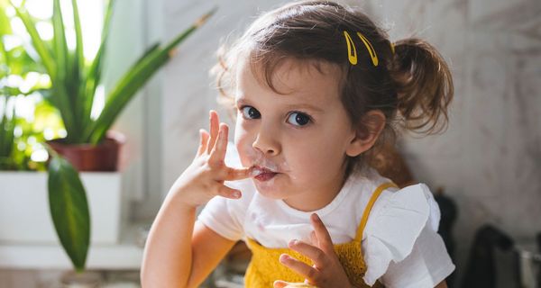 Kleines Mädchen isst Schlagsahne mit den Fingern.